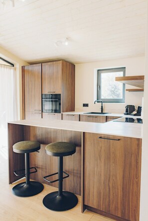 A modern kitchen with wooden cabinets, a central island with stools, and a window providing natural light.