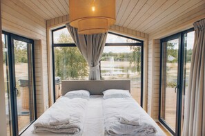 Un dormitorio con cama, ventanas amplias y vistas a un lago.