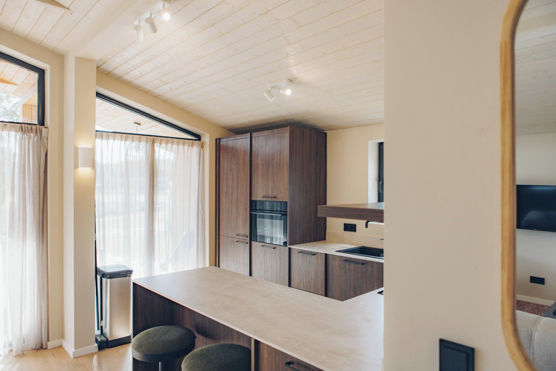 A modern kitchen with wooden cabinets, a built-in oven, and a bar area with stools.