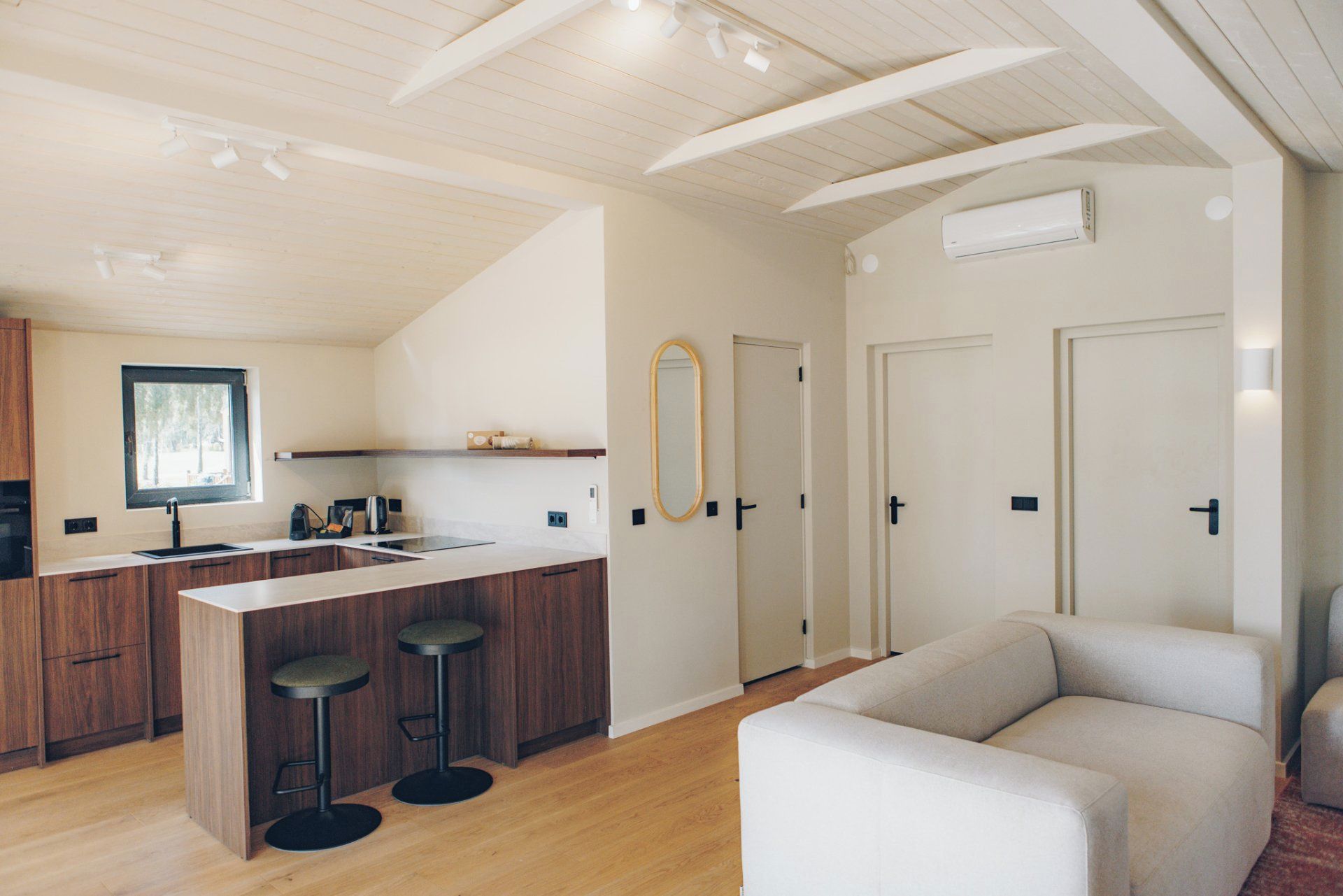A modern kitchen with a central island, bar stools, a window, and a mirror on the wall.