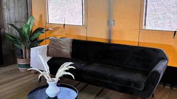 Une pièce avec un canapé noir, une table ronde sur laquelle est posé un vase blanc, et une plante en pot.