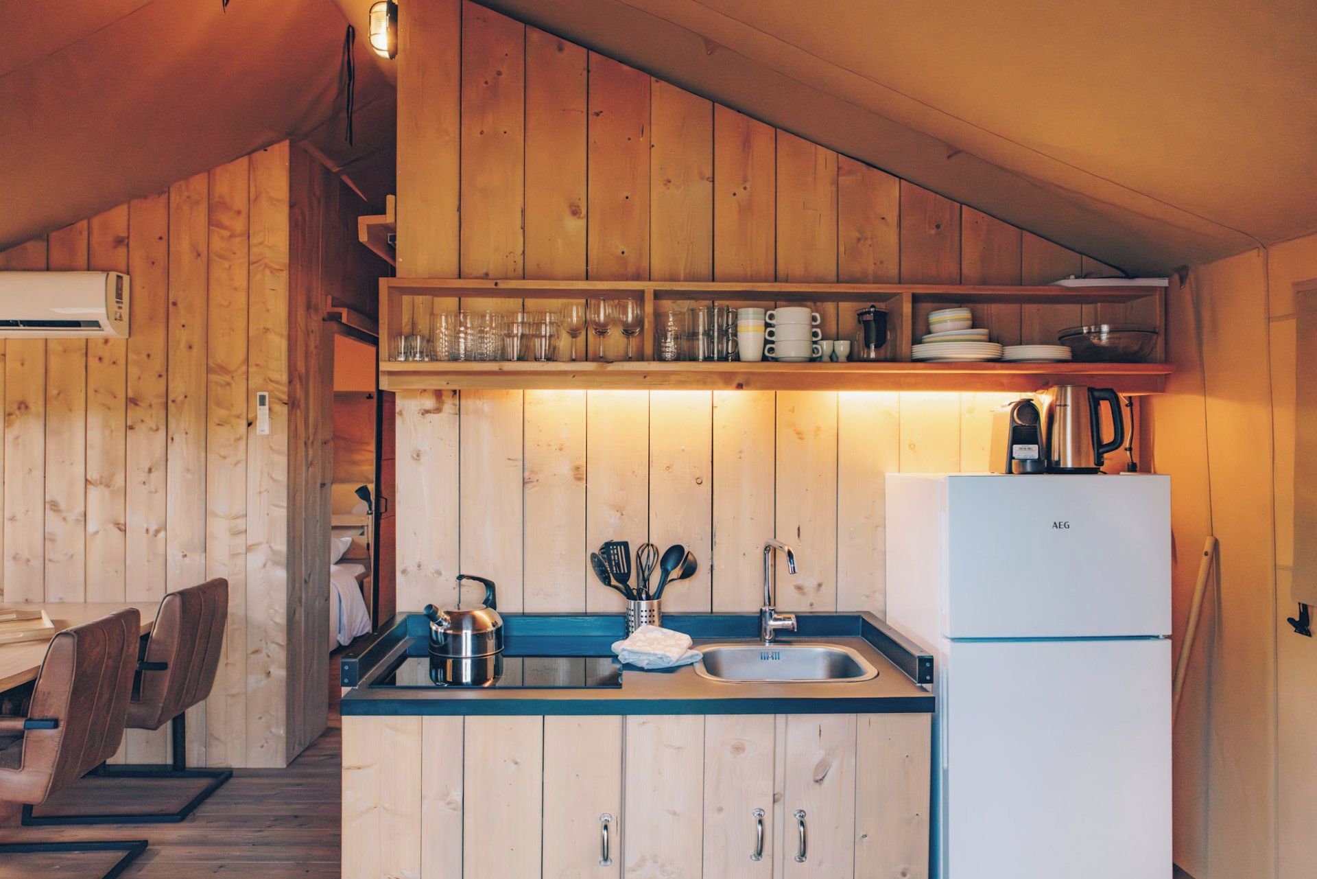 A compact kitchen with wooden cabinets, a sink, a kettle, and a white refrigerator.