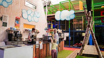 Un espace de jeux pour enfants comprenant une structure d’escalade, une table à jeux et un comptoir avec un menu.