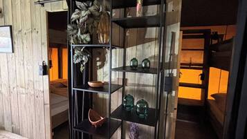 Une pièce avec un mur en bois, une étagère noire ornée d’objets décoratifs et un lit avec une tête de lit.