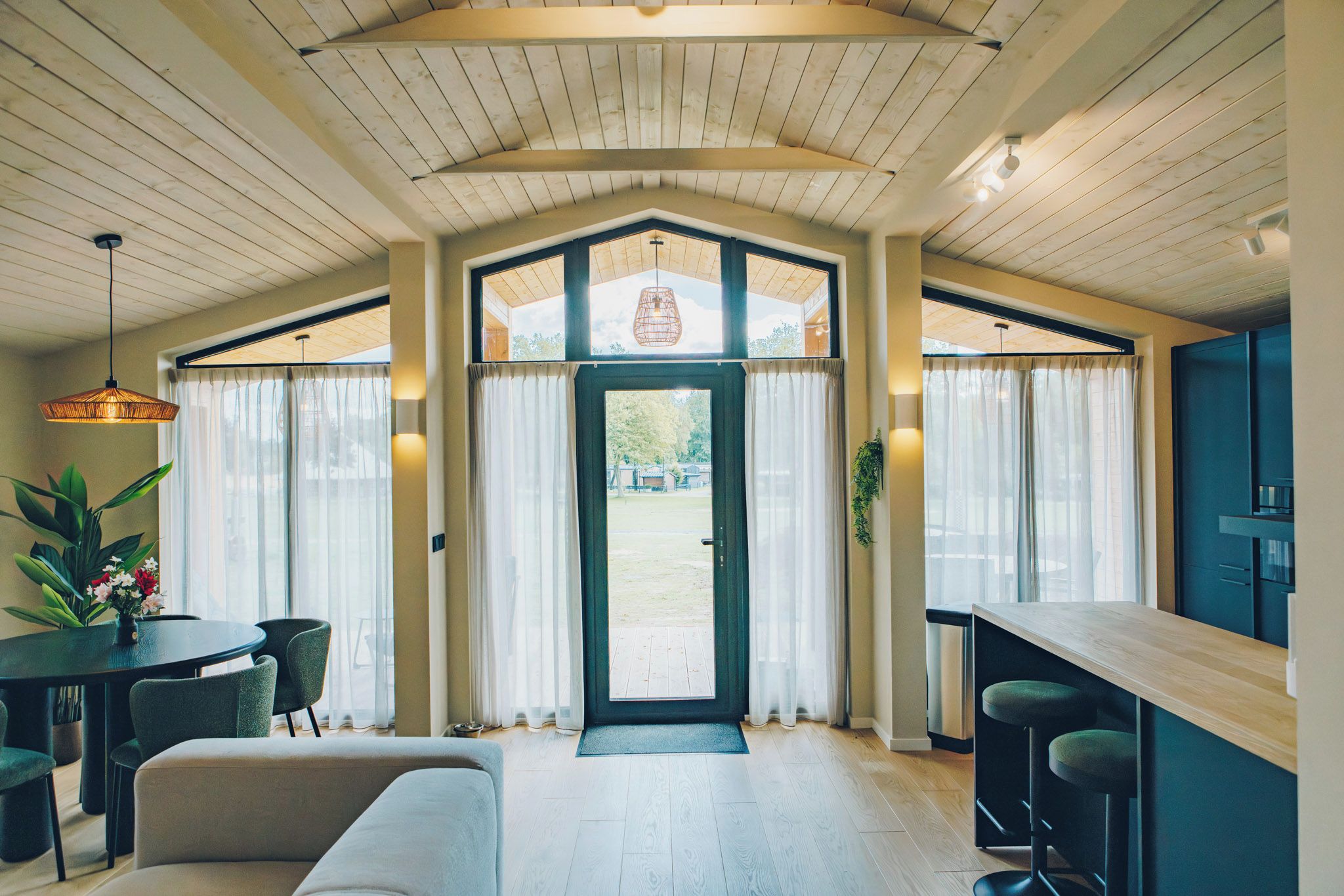 Ein geräumiger Raum mit einer großen Holzbalkendecke, einem Essbereich mit Tisch und Stühlen sowie Blick durch eine Glastür ins Freie.