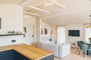 Een moderne woonkamer met een houten eettafel, witte banken en een flatscreen televisie aan de muur.