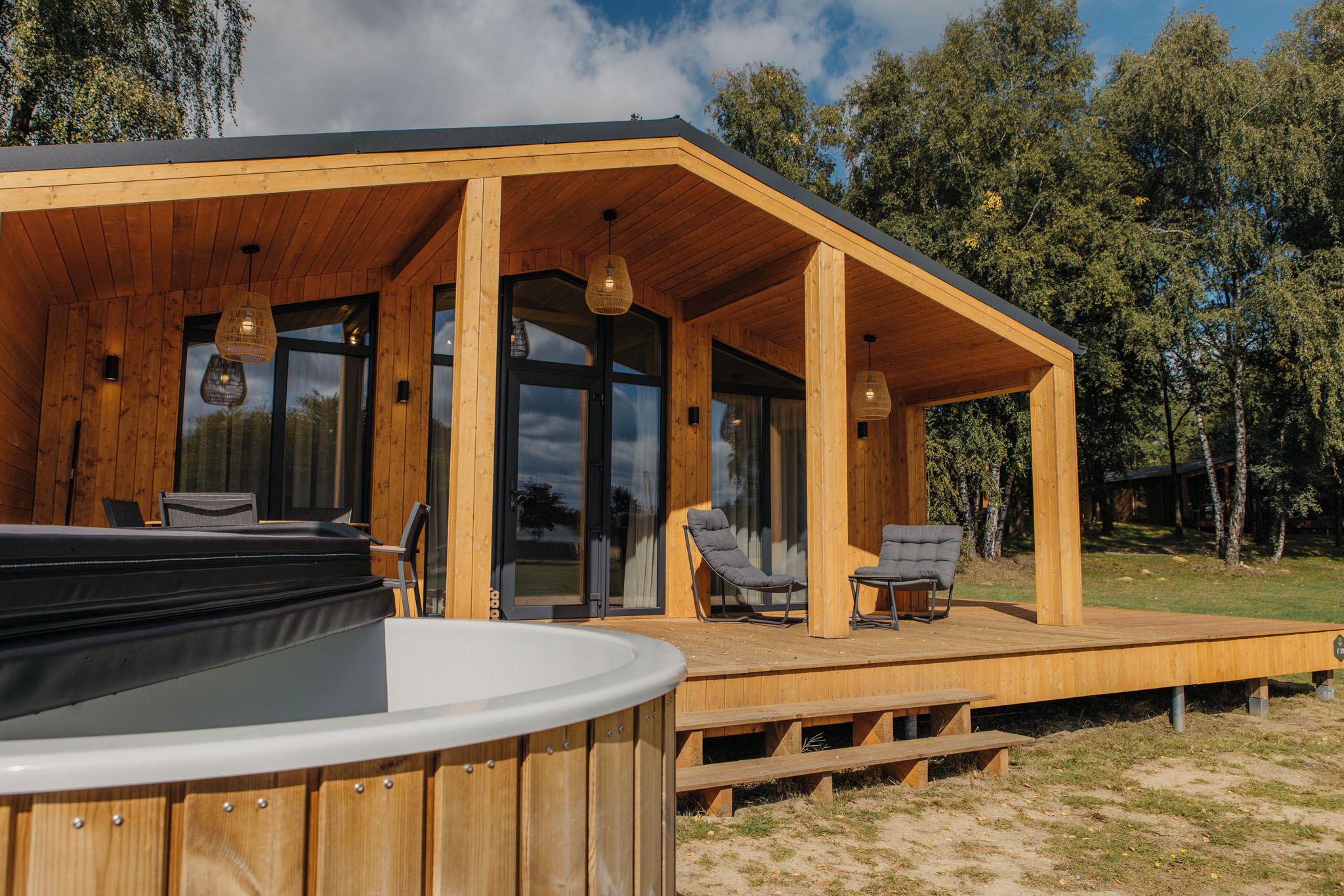 Eine Holzhütte mit Whirlpool, Sitzgelegenheiten im Freien und großen Fenstern.
