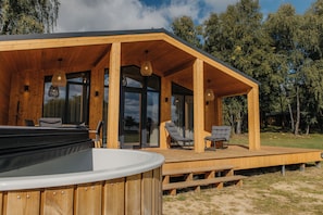 A wooden cabin with a hot tub, outdoor seating, and large windows.