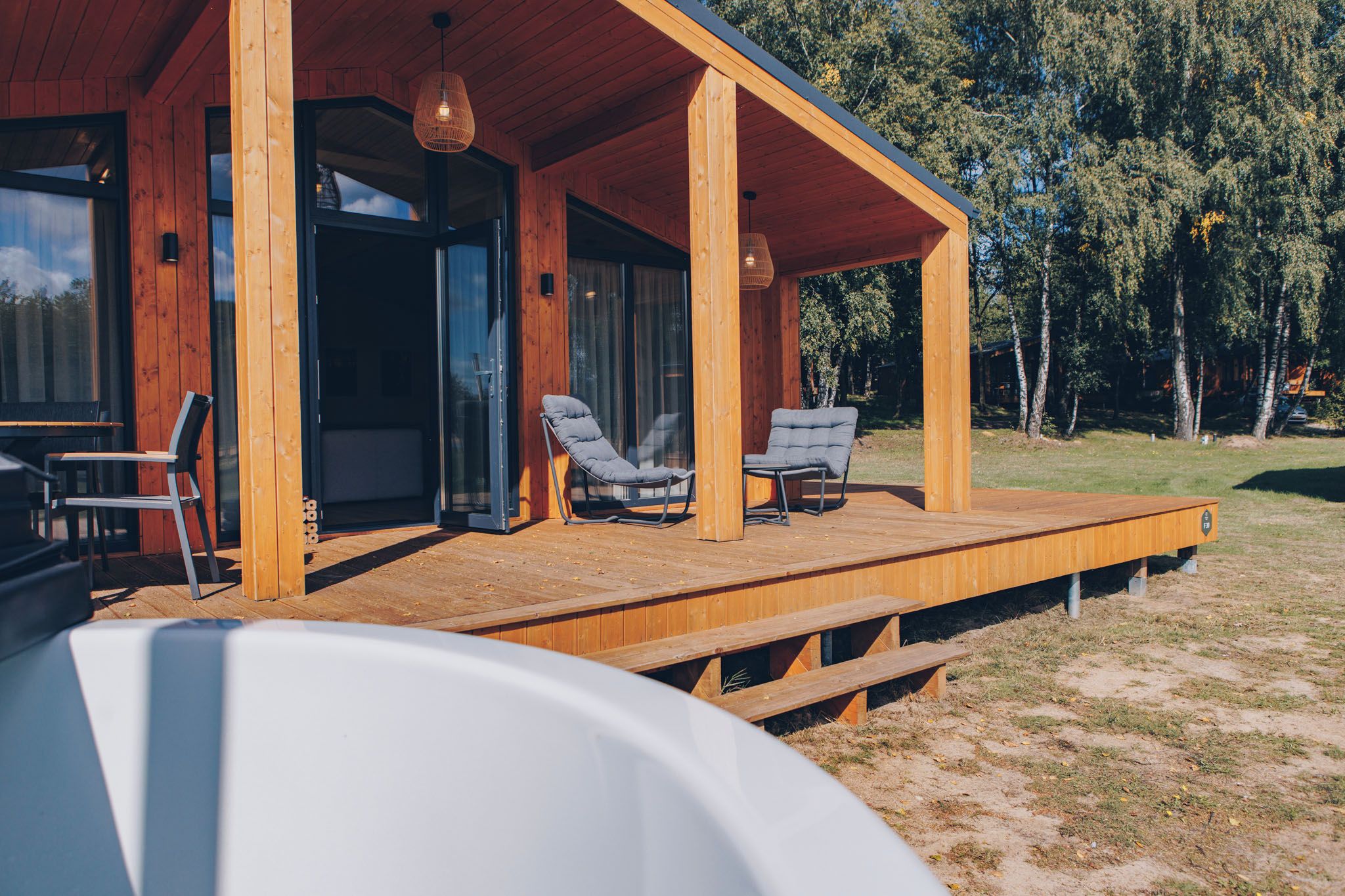 Eine Holzblockhütte mit überdachter Veranda, zwei Liegestühlen und einem Esstisch.