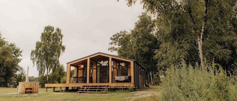 Una cabaña de madera con terraza, rodeada de árboles y pasto.