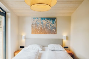 A bedroom with a bed, two bedside tables, a wall-mounted painting, and a ceiling light fixture.
