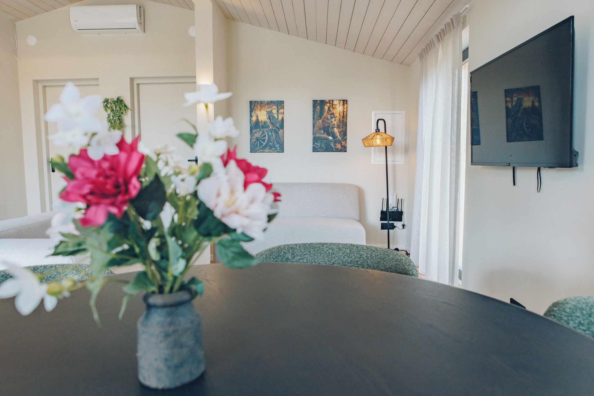 Een moderne hotelkamer met een bed, een tafeltje met bloemen, een lamp en kunst aan de muur.