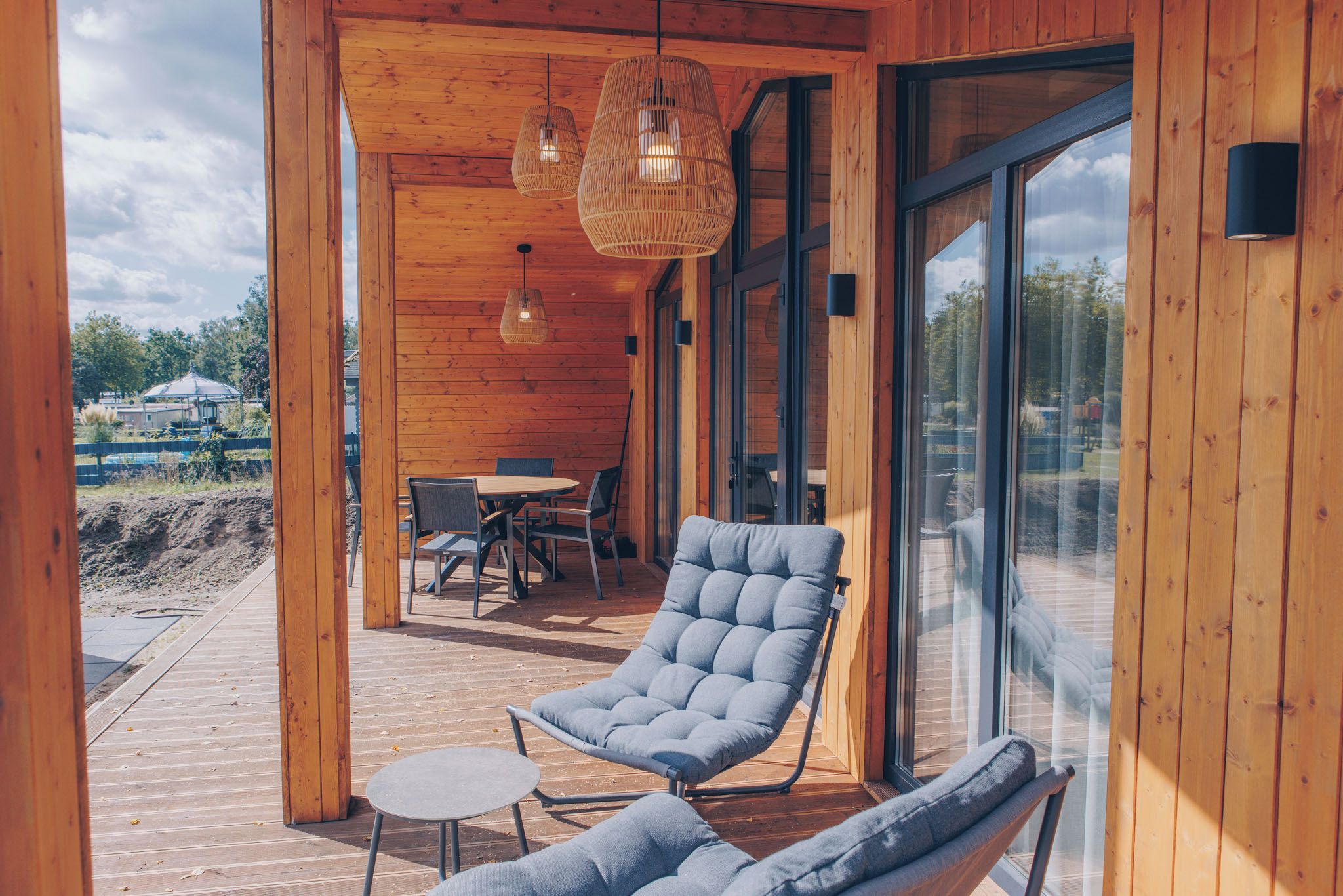 Een houten chalet met een glazen deur, een comfortabele lounge stoel, een klein tafeltje en een hanglamp.