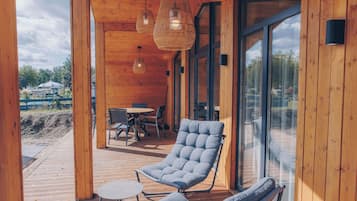 Een houten chalet met een glazen deur, een comfortabele lounge stoel, een klein tafeltje en een hanglamp.
