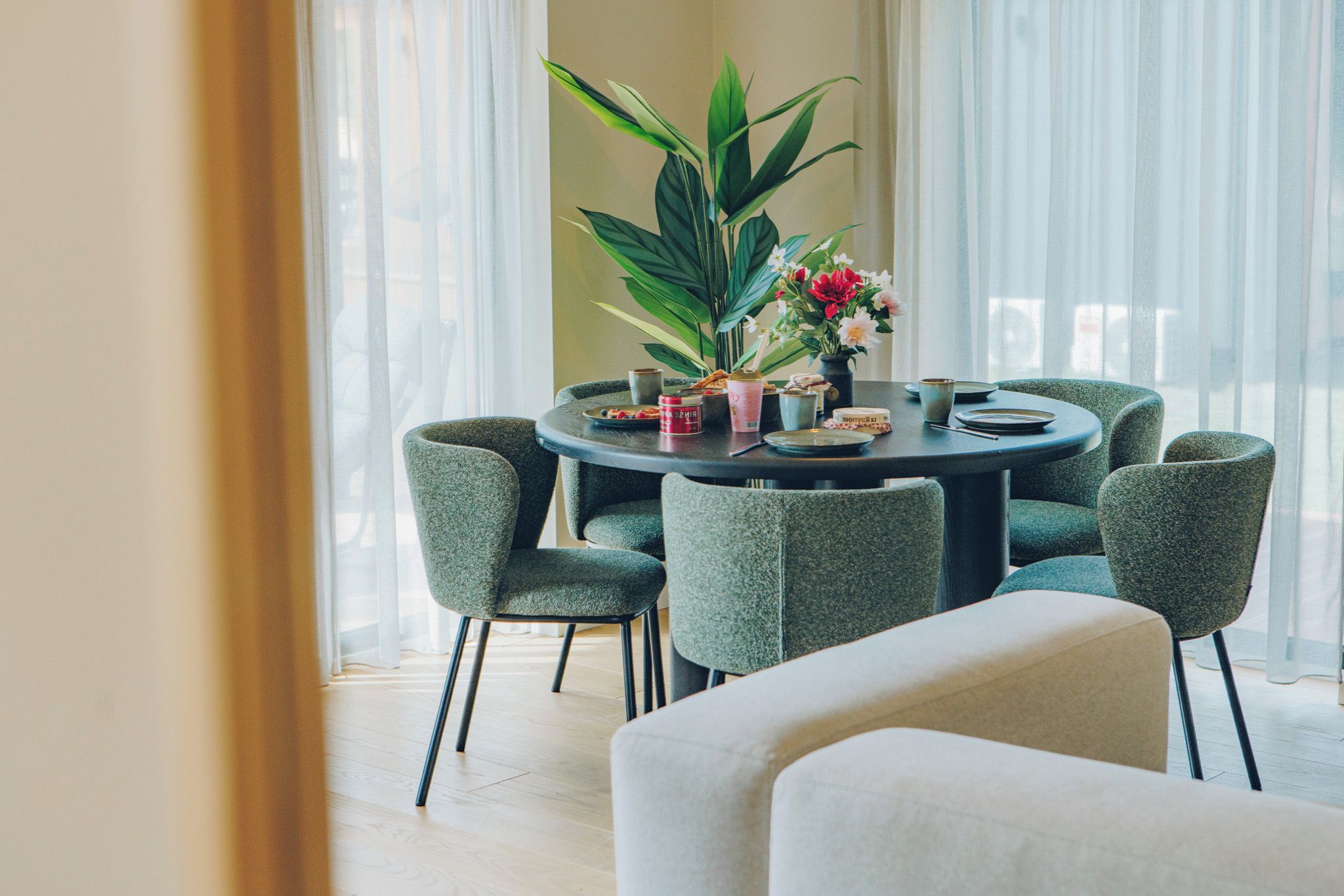 Een ronde eettafel met zes stoelen, een potplant en een vaas met bloemen.