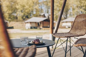 A dining table with two glasses and a plate of food, surrounded by wicker chairs on an outdoor deck.