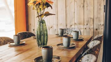 Uma mesa de jantar de madeira com um vaso de vidro contendo flores, rodeada por cadeiras e pratos com xícaras.