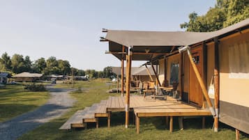 Ein Campingplatz mit einer Holzterrasse, einem überdachten Bereich mit Tisch und Stühlen sowie einer Zeltkonstruktion.