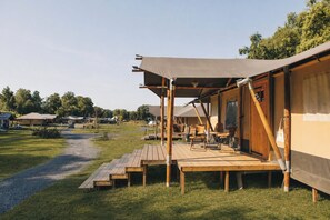 A campsite with wooden deck seating, a covered area with a table and chairs, and a tent structure.