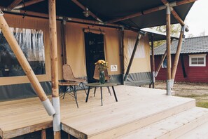 Una terraza de madera con una mesa y sillas, un florero con flores, y un edificio rojo al fondo.