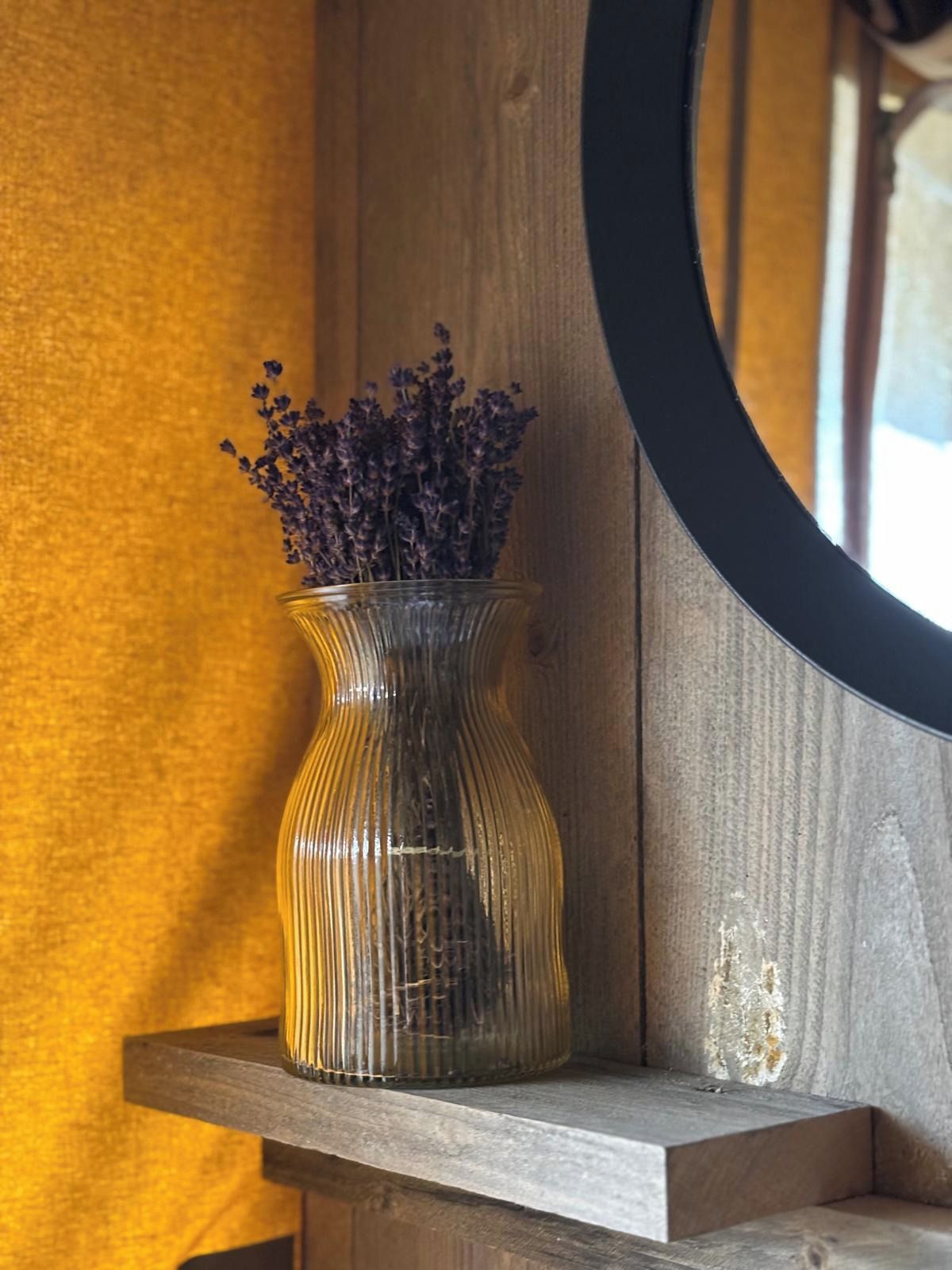 En genomskinlig glasvas med torkad lavendel på en hylla av trä.
