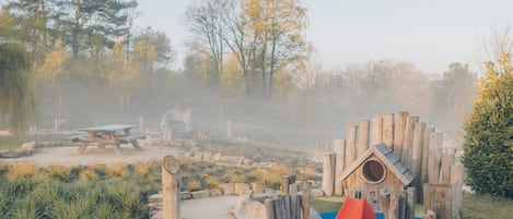 Un espace de jeux avec une structure en bois, un mur d’escalade rouge et une table de pique-nique, le tout situé dans un parc.