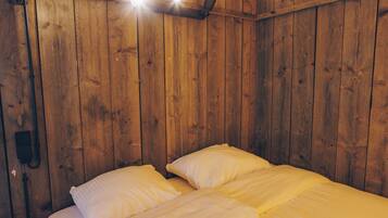 A wooden room with a bed, two wall-mounted lights, and a small shelf.