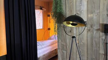 Ein Zimmer mit einem Bett, einer hängenden Pflanze, einer Stehlampe und einem Vorhang.