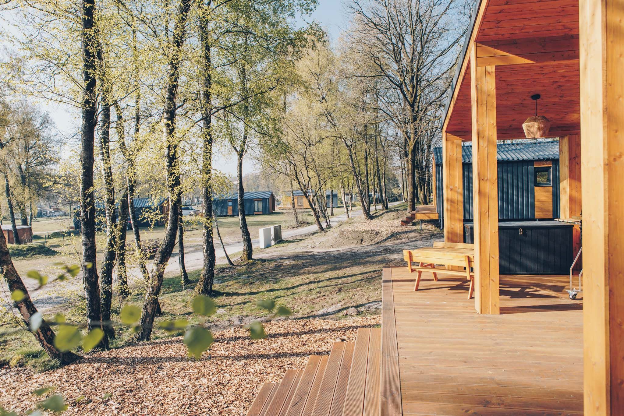 A wooden deck with a bench and a table, surrounded by trees and a view of cabins.
