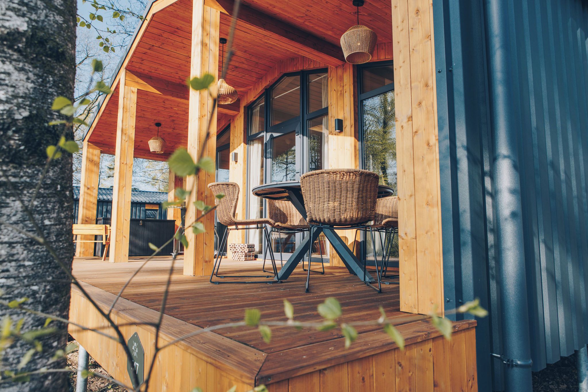 Eine Holzterrasse mit Korbmöbeln und einer Glastür, die zu einem Innenraum führt.