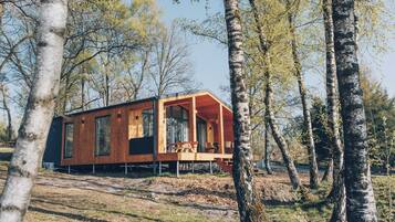 A modern wooden cabin with large windows, a deck, and a natural forest setting.