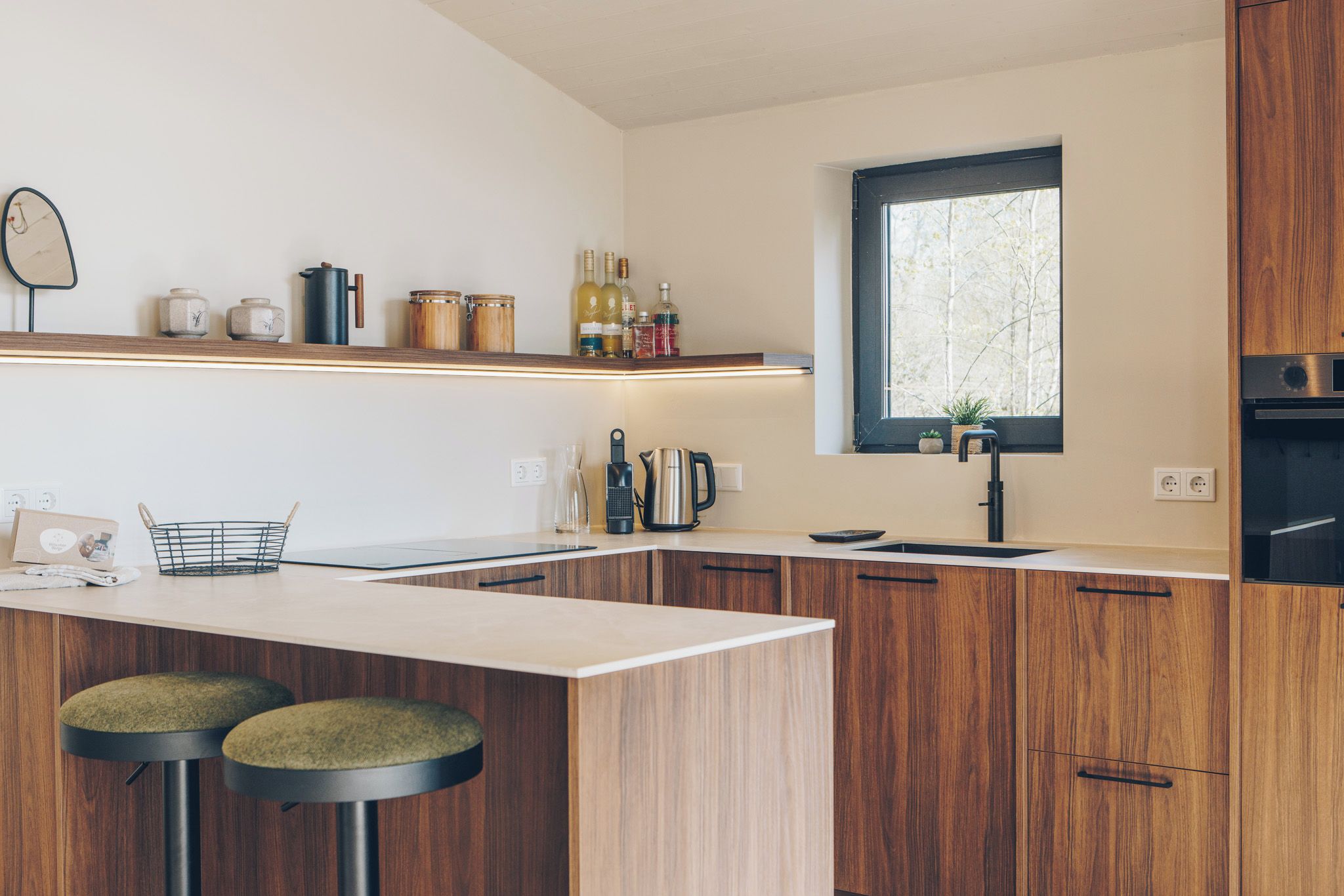 A modern kitchen with wooden cabinets, a central island with stools, a window with a view, and various kitchen appliances.