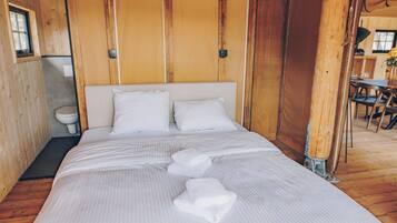 Ein ordentlich bezogenes Bett mit weißen Leinen und Kissen, ein Holzboden und ein kleines Fenster.
