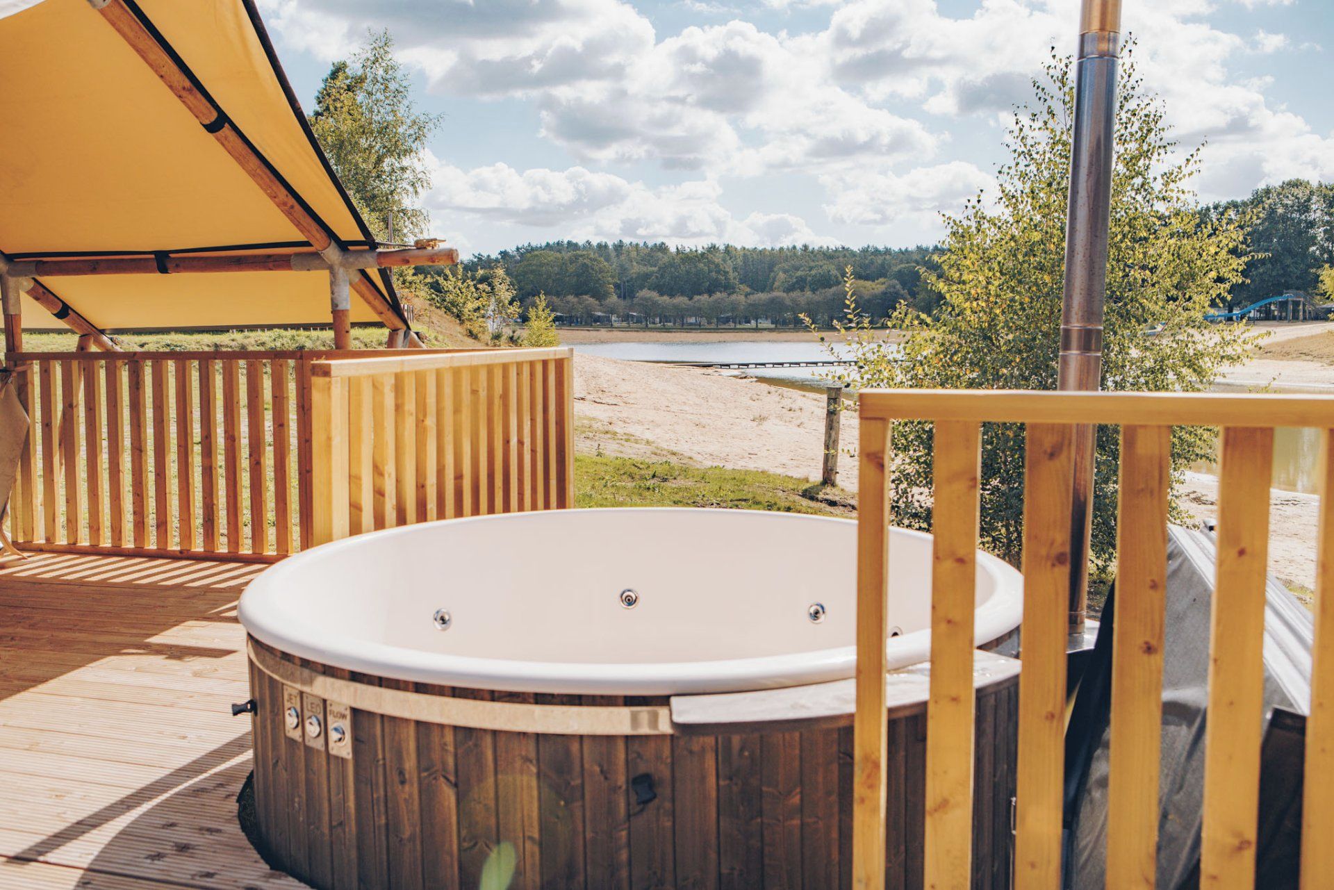A hot tub on a wooden deck with a view of a lake and trees.