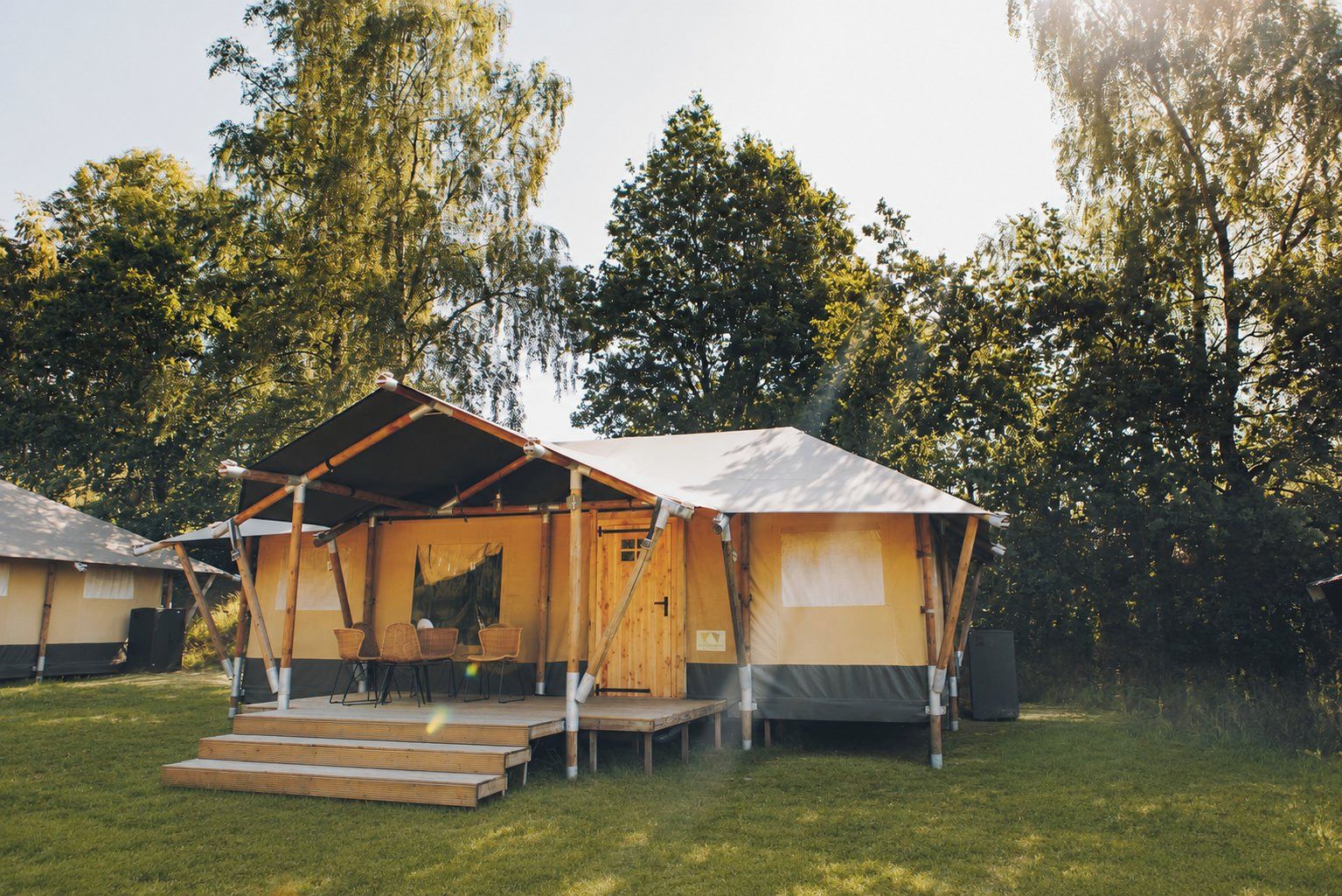 A single-room tent with a wooden deck and a table with chairs, surrounded by trees.