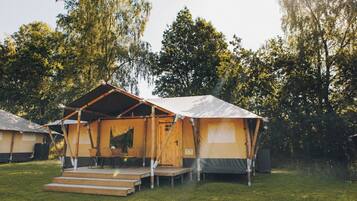 A single-room tent with a wooden deck and a table with chairs, surrounded by trees.