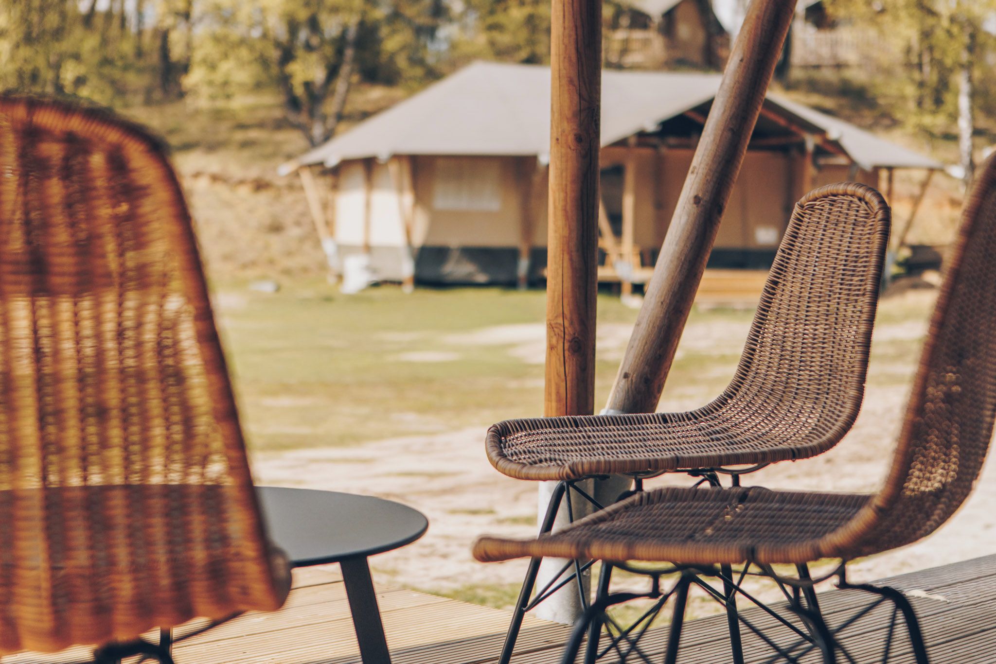 Wicker chairs with metal frames on a wooden deck, a small round table, and a building in the background.