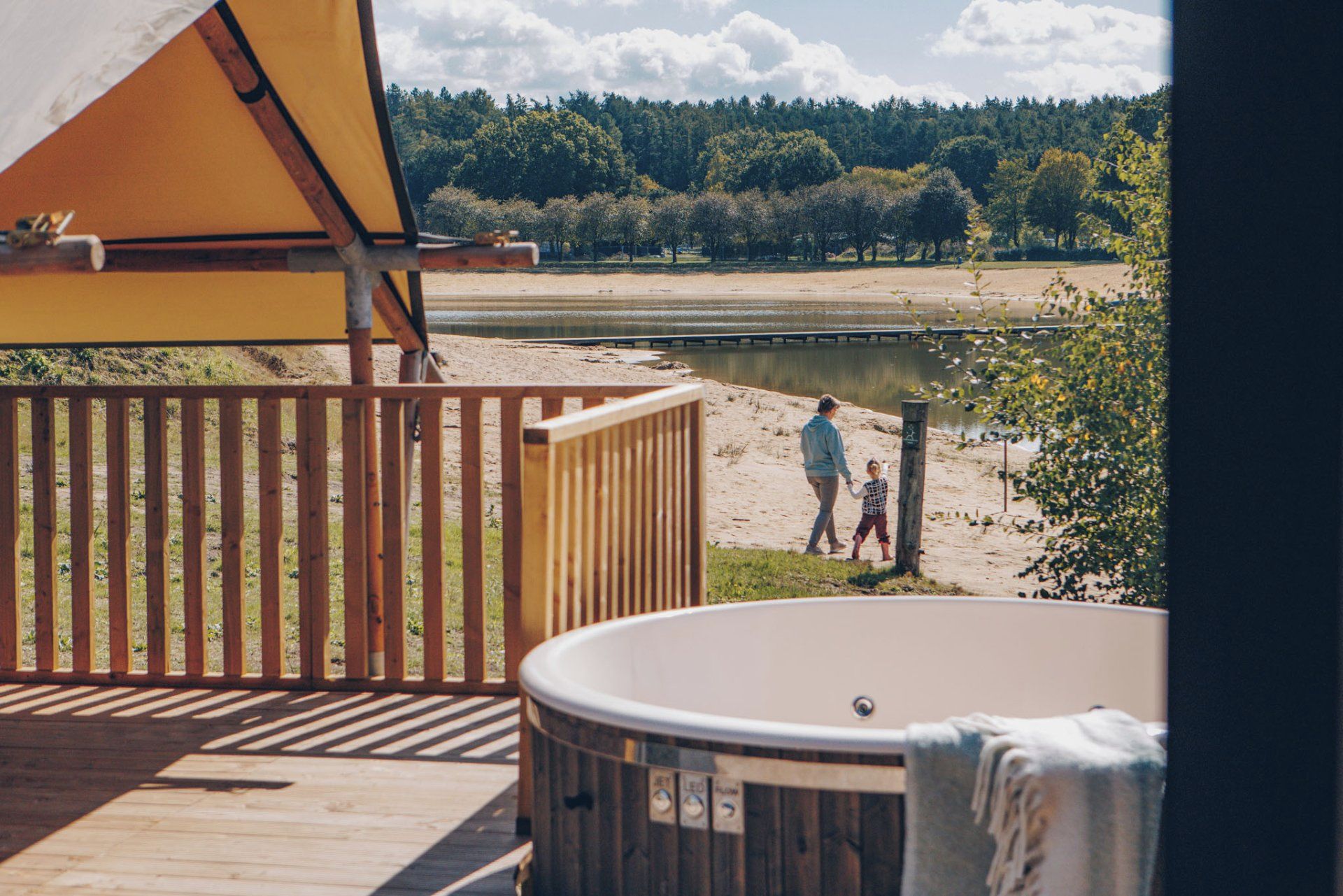 Eine Holzterrasse mit Whirlpool, mit Blick auf einen See und einen bewaldeten Hintergrund.
