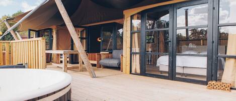 A wooden deck with a hot tub, a dining table, and a sofa.