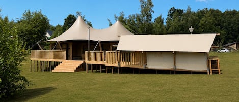 A series of tents with wooden decks and stairs, set in a grassy area with trees in the background.