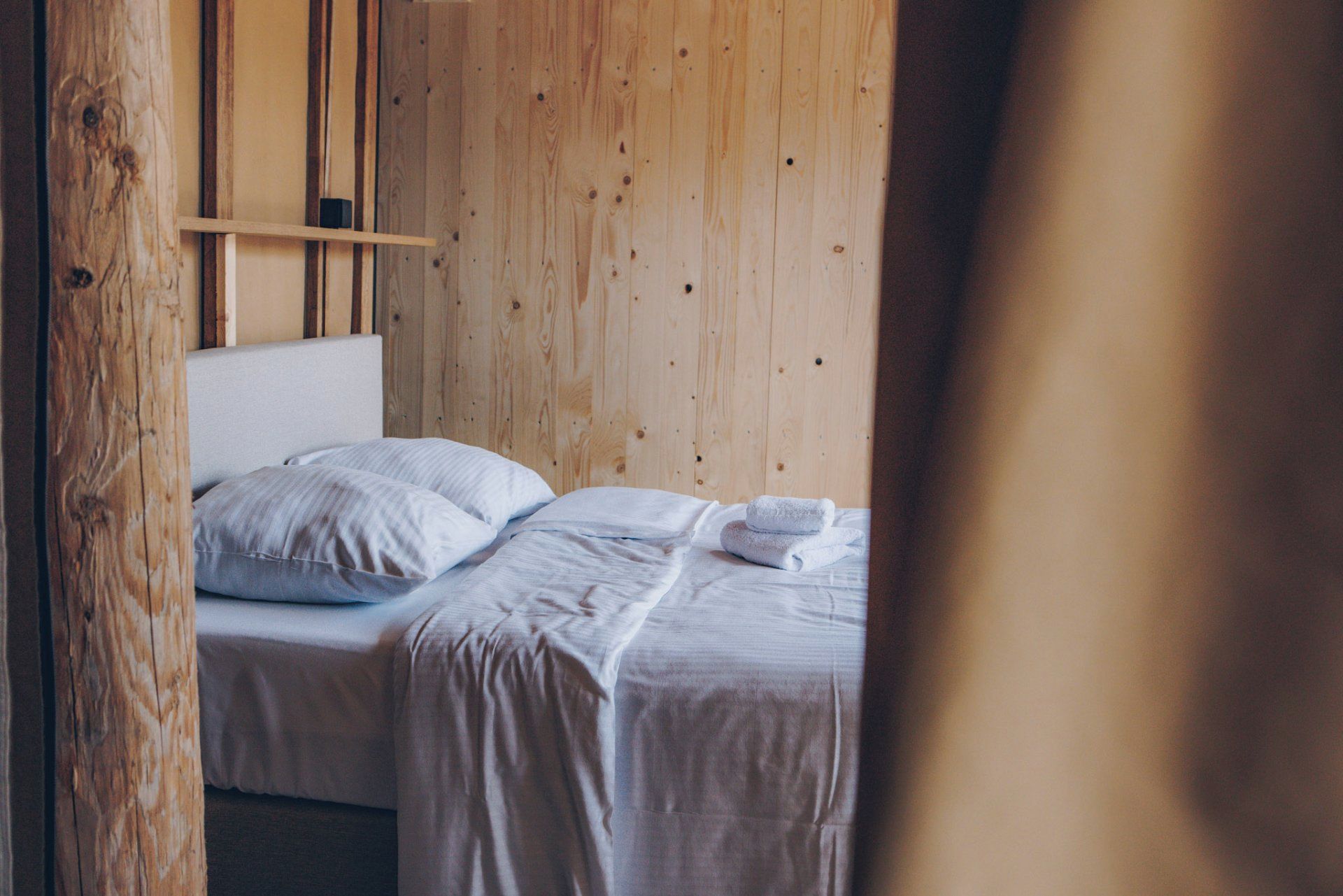 Ein Einzelbett mit weißer Bettwäsche und Kissen, ein Holz-Kopfteil und eine Holzwand.