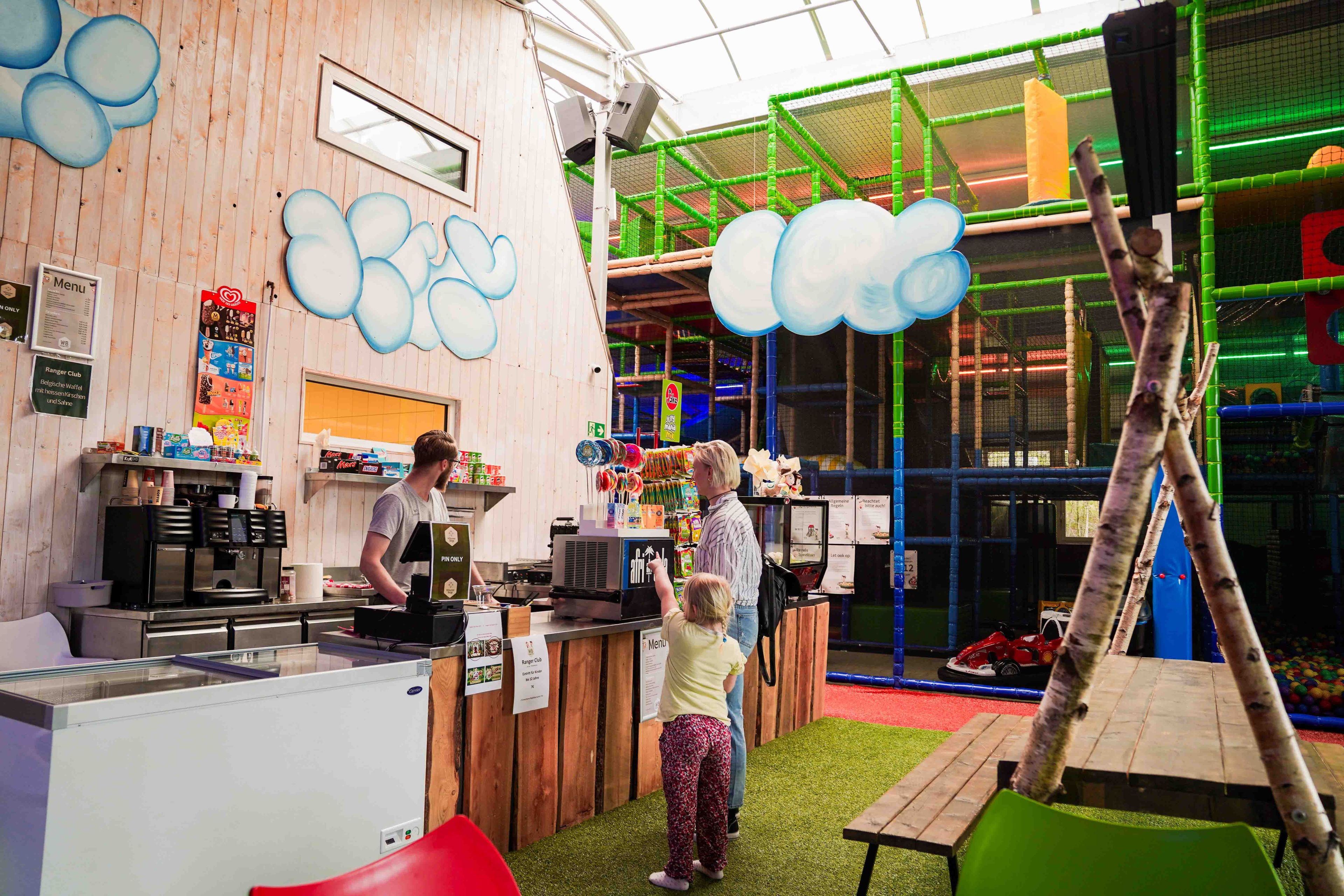 Un espace de jeux pour enfants comprenant une structure d’escalade, une table à jeux et un comptoir avec un menu.