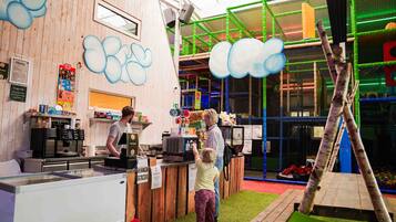 Un espace de jeux pour enfants comprenant une structure d’escalade, une table à jeux et un comptoir avec un menu.