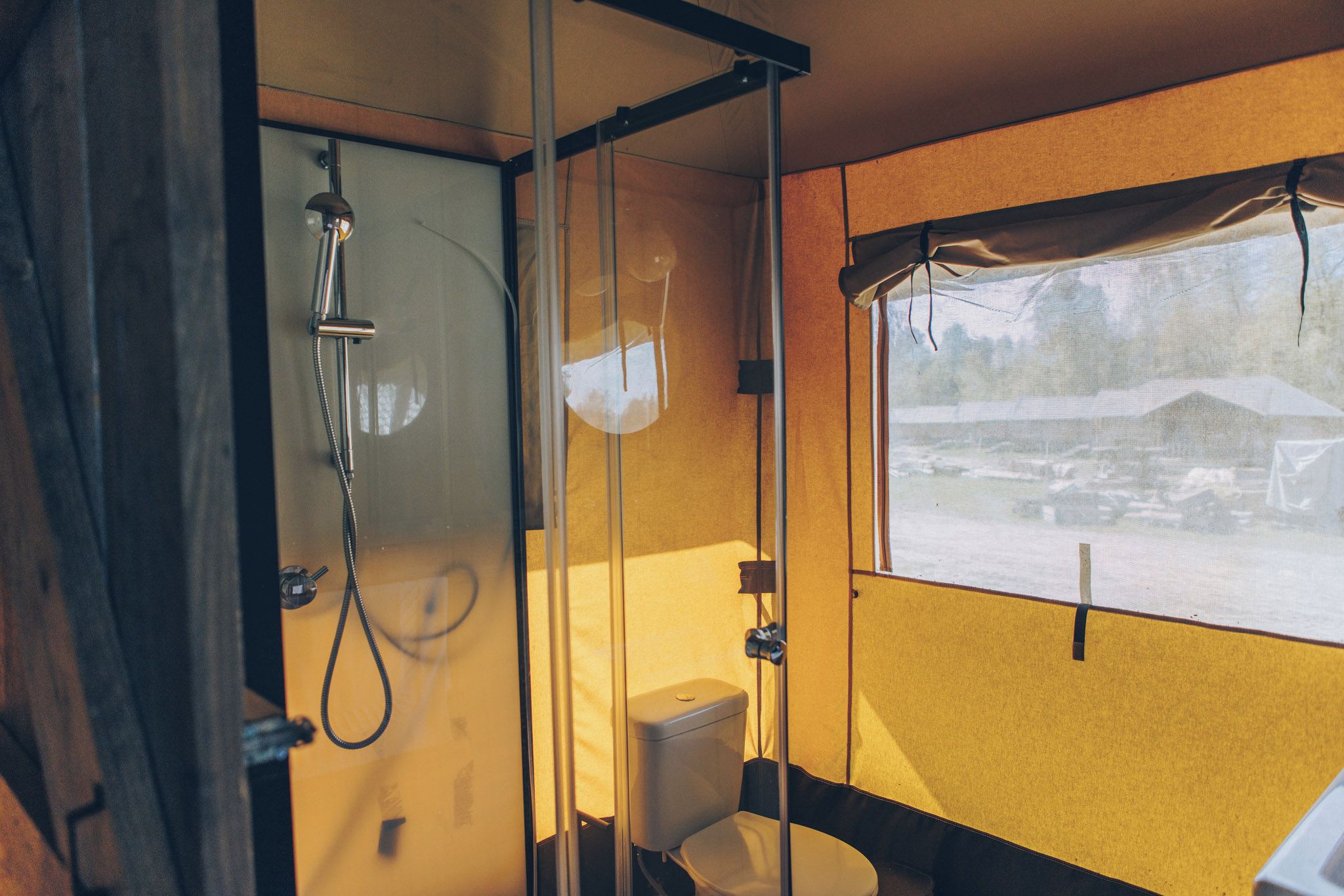 Ein kleines Badezimmer mit Dusche, Toilette und einem Fenster mit Blick auf eine verschneite Landschaft.