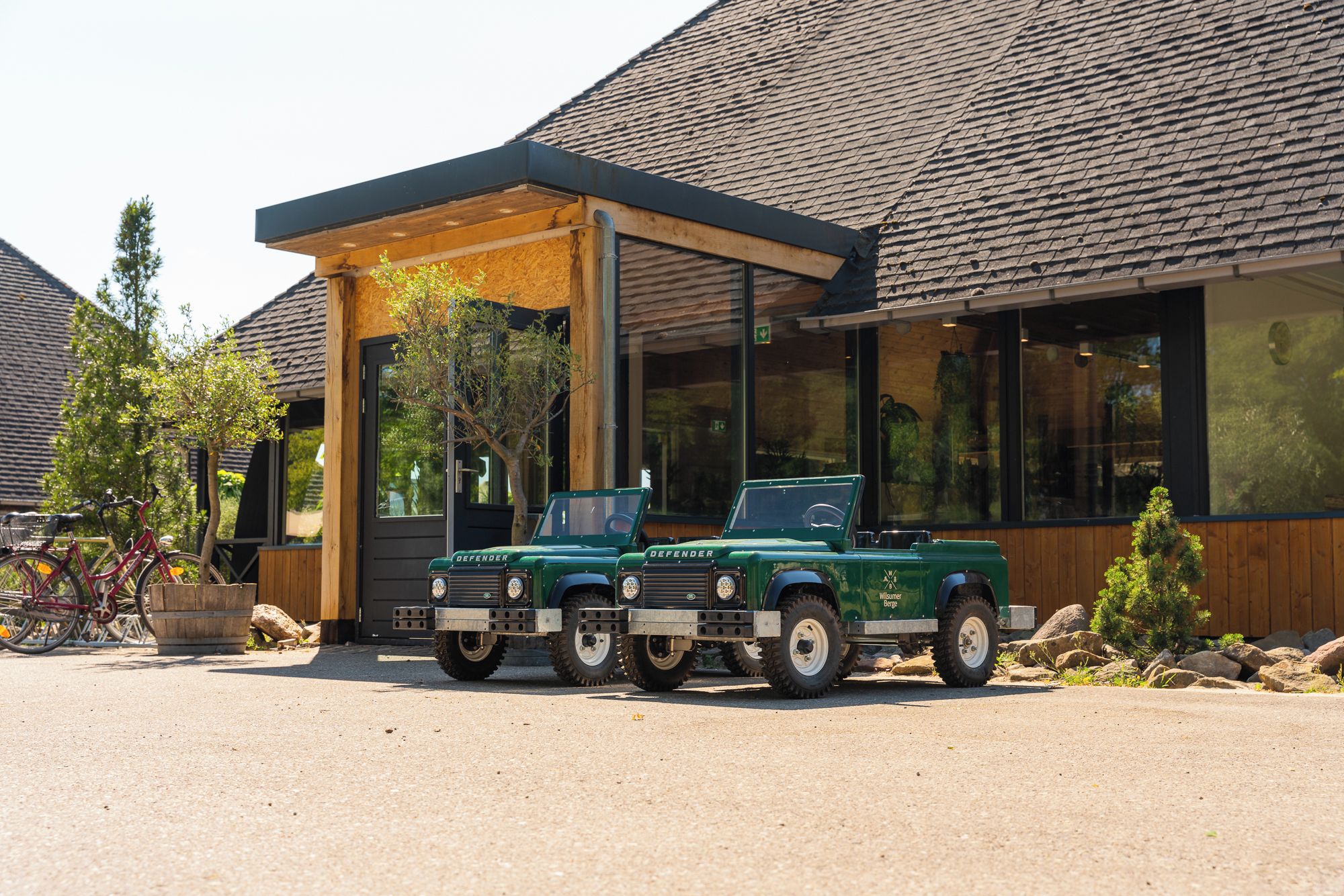 Deux véhicules Defender verts sont stationnés devant un bâtiment doté d’un patio couvert.