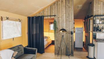 A cozy room with a bed, a sofa, a kitchenette, and a wooden wall.