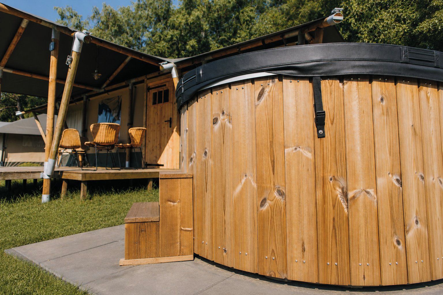 A wooden hot tub with a black cover, a wooden deck with chairs, and a covered outdoor area.