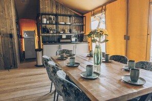 Una mesa de comedor de madera con platos y tazas de cerámica, un florero con flores y una cocina al fondo.