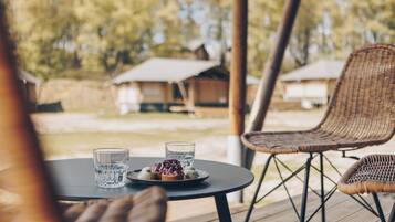 Une table à manger avec deux verres et une assiette de nourriture, entourée de chaises en osier sur une terrasse extérieure.