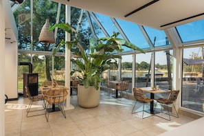Un espacio interior amplio con ventanas grandes, muebles de mimbre y una planta en maceta.